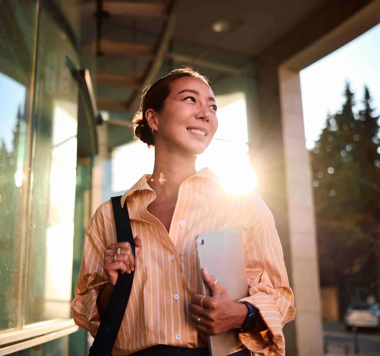 association professional carrying a laptop, standing in the sun, smiling and looking ahead to the future